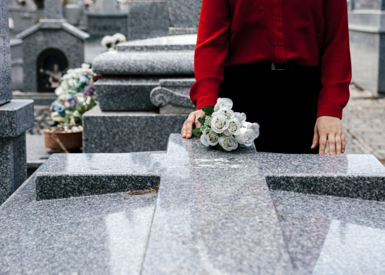 Woman in red blouse putting flowers to a loved one in the cemetery.